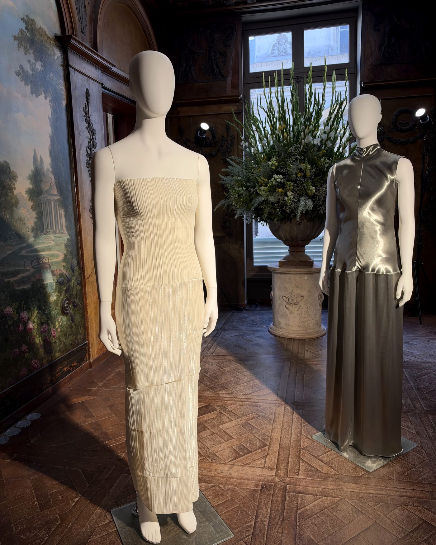 Two gowns on mannequins in a painted Parisian salon